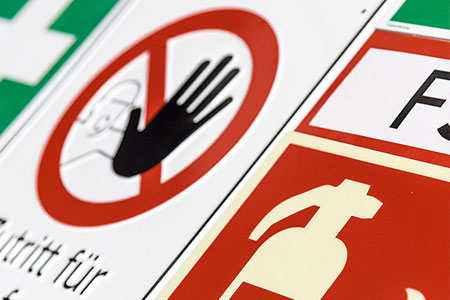 Eine Sammlung verschiedener Sicherheitsschilder, darunter ein Zutrittsverbotsschild mit einer Hand, ein Feuerlöschersymbol und ein Notausgangsschild in mehreren Farben.